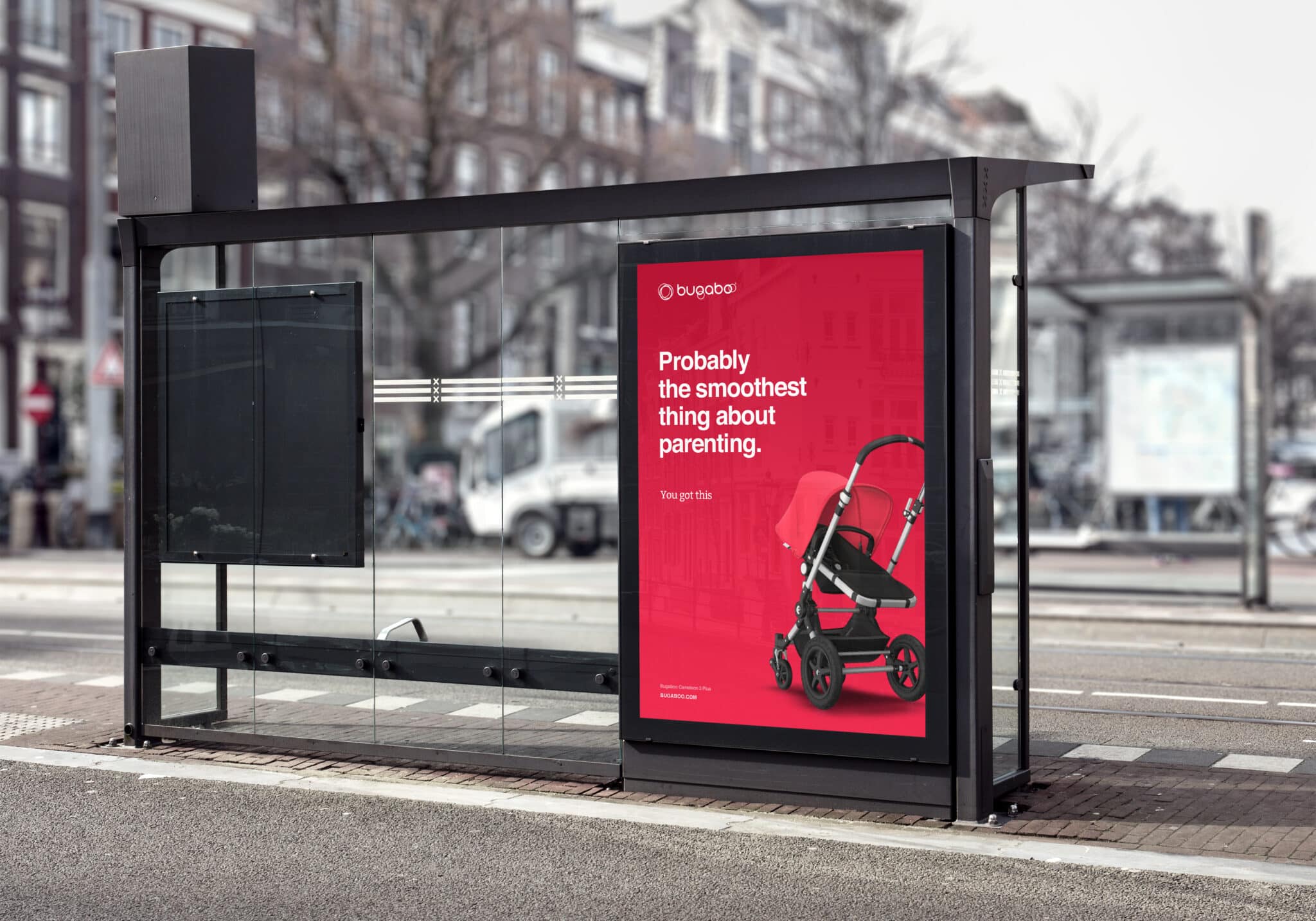A bus stop with a glass enclosure and a bright red advertisement on the right showcasing Bugaboo. The ad, part of a savvy marketing campaign, features a stroller and the text, "Probably the smoothest thing about parenting. Stroller not included. Terms apply." Urban street background is slightly blurred.
