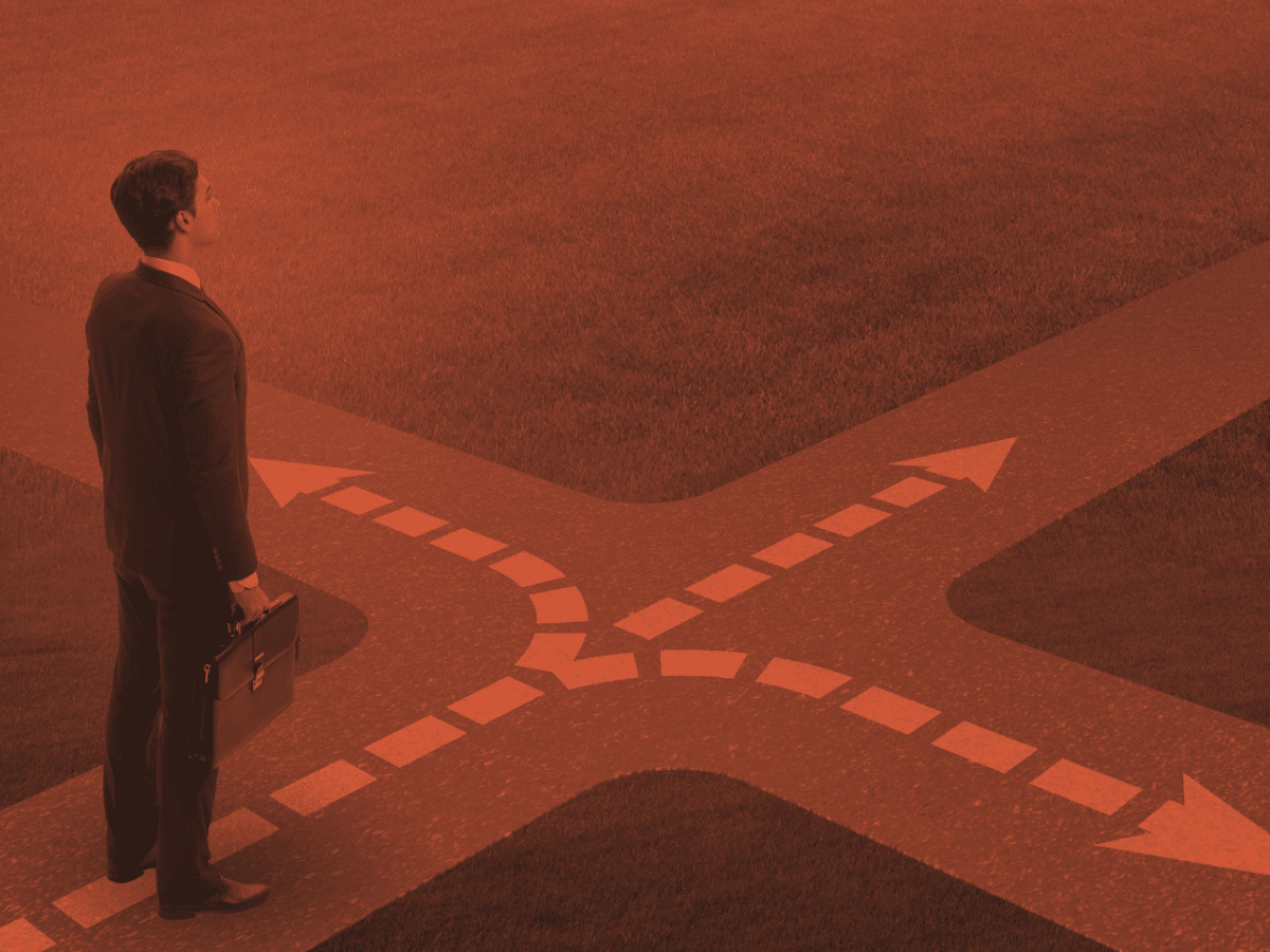 A man in a suit holding a briefcase stands at a crossroads with two divergent paths marked by white dashed lines and arrows on the ground. The image has a red overlay, creating a dramatic effect, symbolizing the uncertainly certain path he faces in his employee experience.