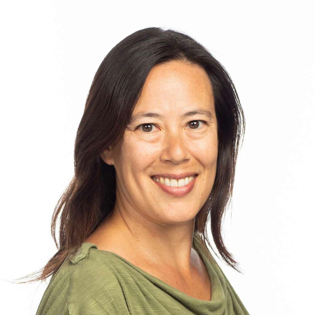 Susan Martindill, a woman with shoulder-length brown hair, smiles warmly at the camera. She is wearing a light green blouse, and the background is a plain white.