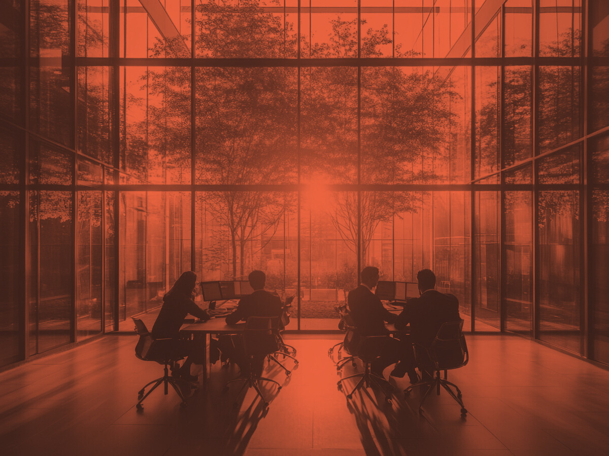 Business professionals in a glass-walled office building working around a table as sunlight streams through trees outside, symbolizing clarity and growth.