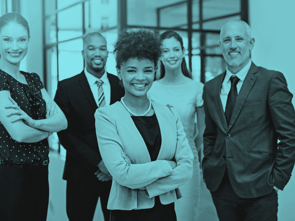 A diverse group of confident business professionals standing together in a modern office, smiling and dressed in professional attire.