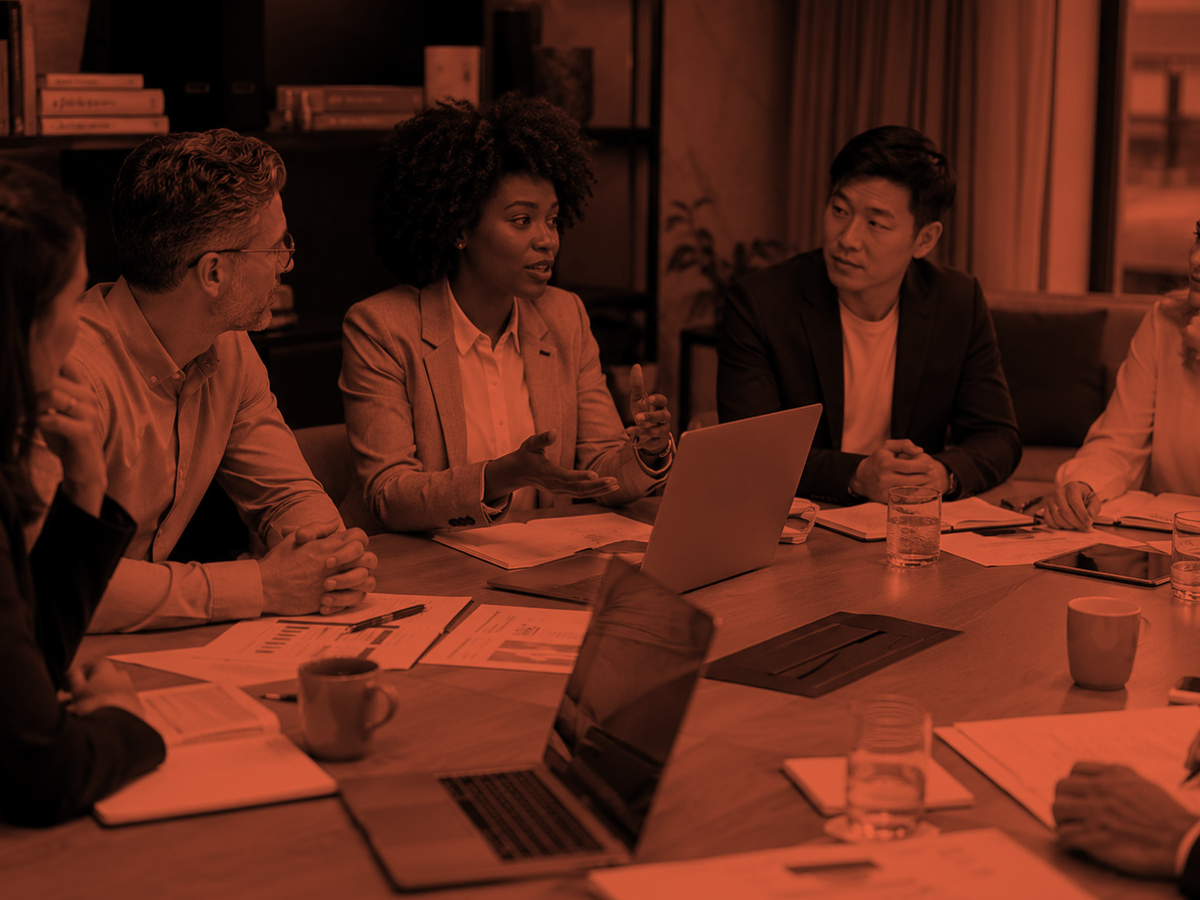 Burnt orange duotone of diverse professionals in a strategy meeting around a conference table, representing cross-functional commercial alignment.