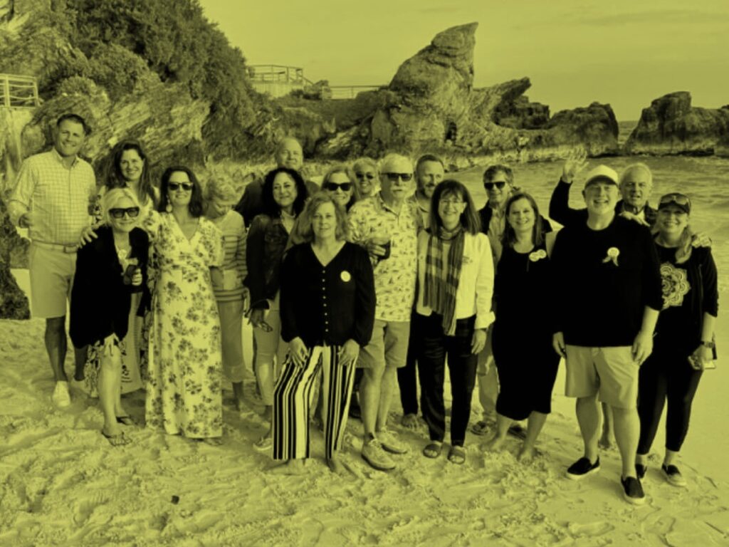 Group of people standing together on a rocky shoreline near the ocean in a yellow duotone image.