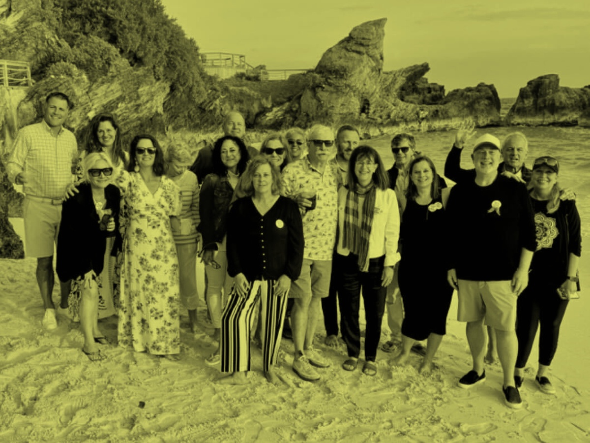 Group of people standing together on a rocky shoreline near the ocean in a yellow duotone image.