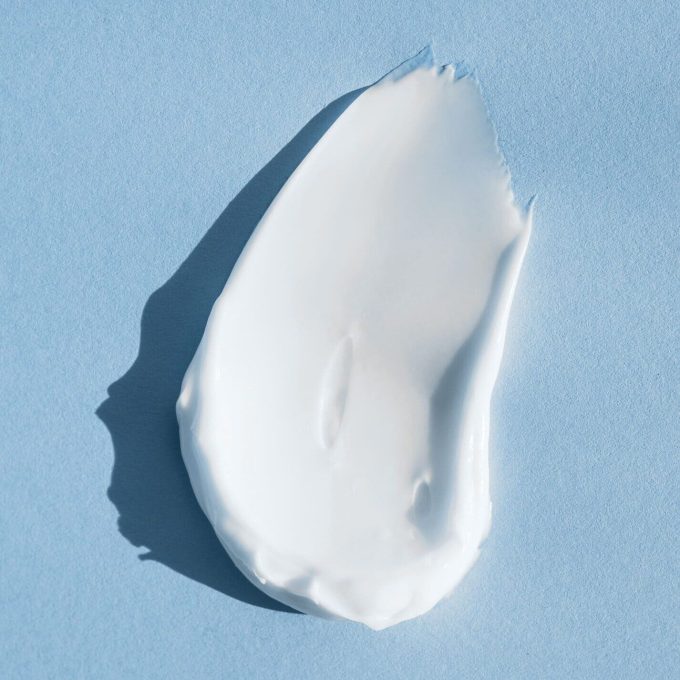 A dab of smooth white cream is spread on a light blue background, highlighting its thick, soft texture, perfect for eCommerce product photography.