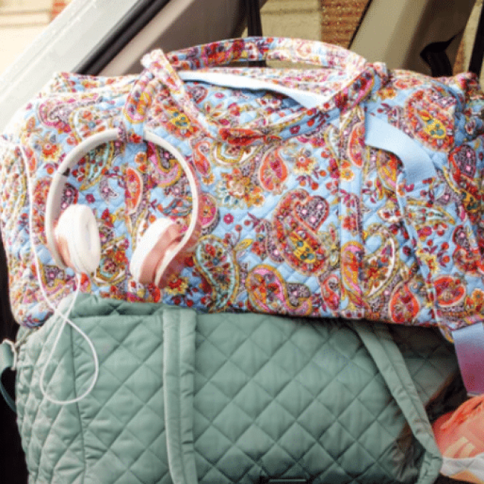 A colorful, paisley-patterned bag with pink and white headphones draped over it sits in a car. Beneath it is a teal, quilted bag. The car's interior, including windows and seats, is visible in the background—a perfect scene curated by our marketing team.